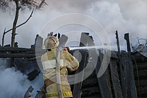 Firefighter extinguishes the fire. Fireman holding hose with water, watering strong stream of burning wooden structure in smoke. photo