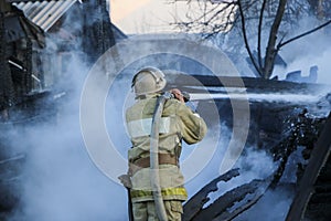 Firefighter extinguishes the fire. Fireman holding hose with water, watering strong stream of burning wooden structure in smoke. photo