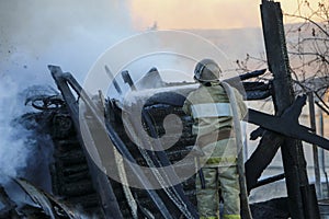 Firefighter extinguishes the fire. Fireman holding hose with water, watering strong stream of burning wooden structure in smoke. photo