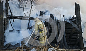 Firefighter extinguishes the fire. Fireman holding hose with water, watering strong stream of burning wooden structure in smoke. photo