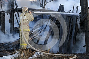 Firefighter extinguishes the fire. Fireman holding hose with water, watering strong stream of burning wooden structure in smoke. photo