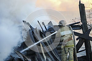 Firefighter extinguishes the fire. Fireman holding hose with water, watering strong stream of burning wooden structure in smoke. photo