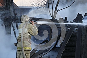 Firefighter extinguishes the fire. Fireman holding a hose with water, watering a strong stream of burning wooden structure in the photo