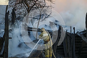 Firefighter extinguishes the fire. Fireman holding hose with water, watering strong stream of burning wooden structure in smoke.