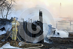 Firefighter extinguishes the fire. Fireman holding hose with water, watering strong stream of burning wooden structure in smoke. photo