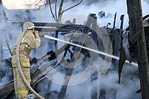 Firefighter extinguishes the fire. Fireman holding hose with water, watering strong stream of burning wooden structure in smoke. photo