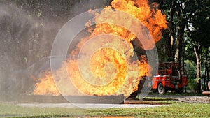 Firefighter fighting with flame using fire hose chemical water foam spray engine. Fireman wear hard hat, body safe suit uniform