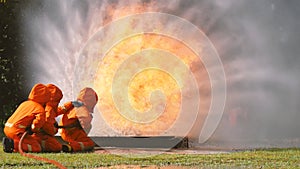 Firefighter fighting with flame using fire hose chemical water foam spray engine. Fireman wear hard hat, body safe suit uniform