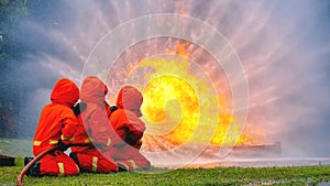 Firefighter fighting with flame using fire hose chemical water foam spray engine. Fireman wear hard hat, body safe suit uniform