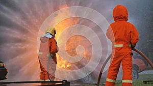 Firefighter fighting with flame using fire hose chemical water foam spray engine. Fireman wear hard hat, body safe suit uniform