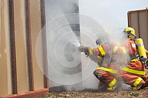 firefighter in fire protection suit spraying water to fire surround with smoke and drizzle