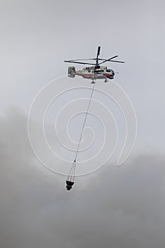 Firefighter helicopter with a water tank in smoke from a fire