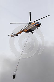 Firefighter helicopter with a water tank in smoke from a fire