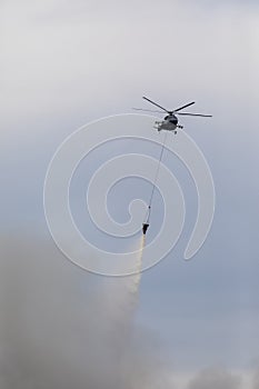 Firefighter helicopter with a water tank in smoke from a fire