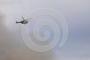 Firefighter helicopter with a water tank in smoke from a fire