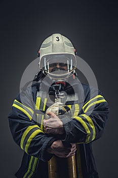 Firefighter in helmet and mask holds oxygen tanks.