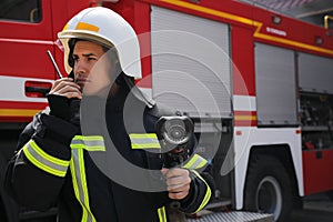 Firefighter with high pressure water jet using portable radio set near fire truck outdoors