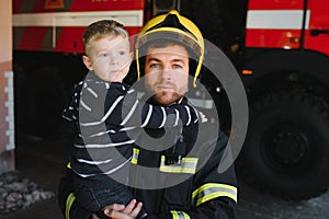 A firefighter take a little child boy to save him. Fire engine car on background. Fireman with kid in his arms