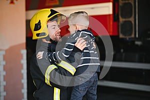 A firefighter take a little child boy to save him. Fire engine car on background. Fireman with kid in his arms