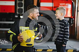 A firefighter take a little child boy to save him. Fire engine car on background. Fireman with kid in his arms