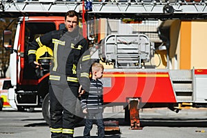 A firefighter take a little child boy to save him. Fire engine car on background. Fireman with kid in his arms