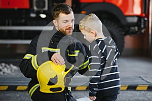 A firefighter take a little child boy to save him. Fire engine car on background. Fireman with kid in his arms