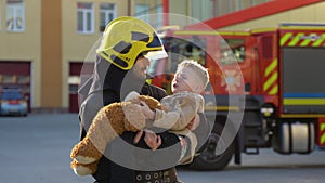 A firefighter take a little child boy to save him. Fireman with kid in his arms. Fire engine car on background