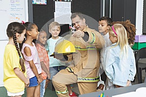 Firefighter teaching student about fire safety while holding fire helmet