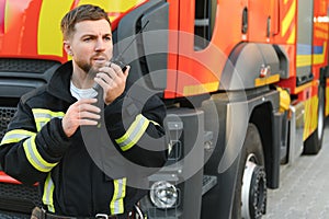 Firefighter in uniform using portable radio set near fire truck outdoors