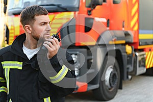 Firefighter in uniform using portable radio set near fire truck outdoors