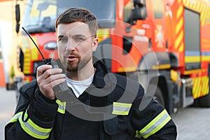 Firefighter in uniform using portable radio set near fire truck outdoors