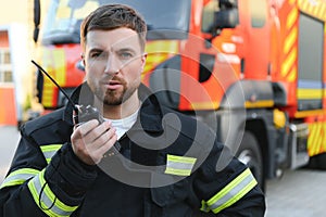 Firefighter in uniform using portable radio set near fire truck outdoors