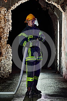 Firefighter using a water hose to eliminate a fire hazard. Team of female and male firemen in dangerous rescue mission.