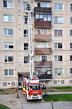 Firefighters in action, a man uprise in telescopic boom basket of fire truck. Block of flats in background.