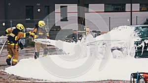 Firefighters extinguish fire from the burning car using foam