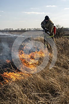 Firefighters extinguish the flames of burning grass