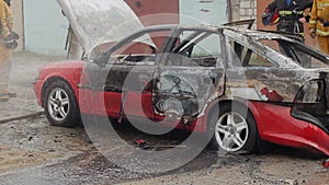 Firefighters or firemen pour water on a burnt car