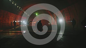 Firefighters inside a dark tunnel with emergency lights in the background