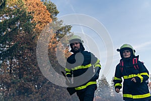 Firefighters man and woman at action, running through smoke with shovels to stop fire in forest.