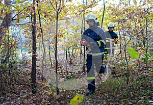 Firefighters men at action, running through smoke with shovels to stop fire in forest.