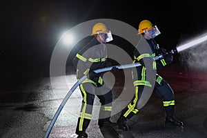 Firefighters use a water hose to eliminate a fire hazard. Team of firemen in the dangerous rescue mission.
