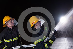 Firefighters use a water hose to eliminate a fire hazard. Team of firemen in the dangerous rescue mission.