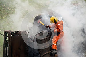 Firefighters using ax destroy obstacles in a burning and smoky car.