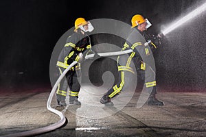 Firefighters using a water hose to eliminate a fire hazard. Team of female and male firemen in dangerous rescue mission