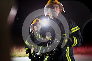 Firefighters using a water hose to eliminate a fire hazard. Team of female and male firemen in dangerous rescue mission