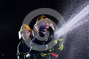 Firefighters using a water hose to eliminate a fire hazard. Team of female and male firemen in dangerous rescue mission