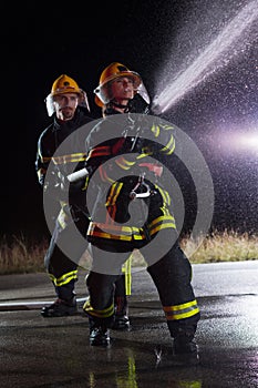 Firefighters using a water hose to eliminate a fire hazard. Team of female and male firemen in dangerous rescue mission