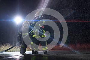 Firefighters using a water hose to eliminate a fire hazard. Team of female and male firemen in dangerous rescue mission