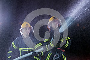 Firefighters using a water hose to eliminate a fire hazard. Team of female and male firemen in dangerous rescue mission