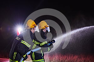 Firefighters using a water hose to eliminate a fire hazard. Team of female and male firemen in dangerous rescue mission